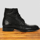 A single black textured lace-up ankle boot with a low block heel, shown in profile on a wooden surface against a light gray background.