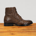 A brown textured leather lace-up ankle boot with a black sole, displayed on a wooden surface against a light gray background.