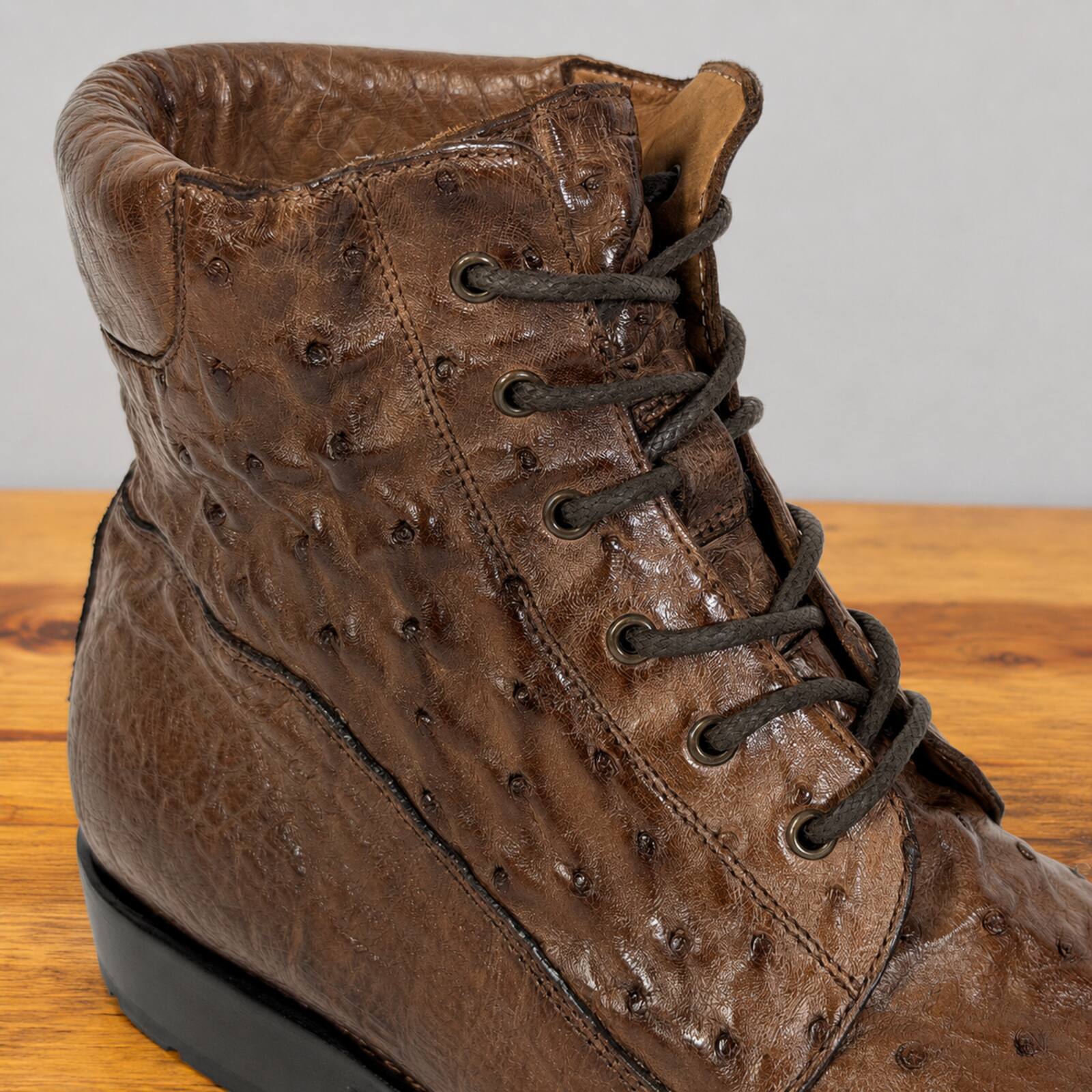 A brown textured lace-up boot with an ostrich-quill pattern, shown on a wooden surface against a neutral gray background.