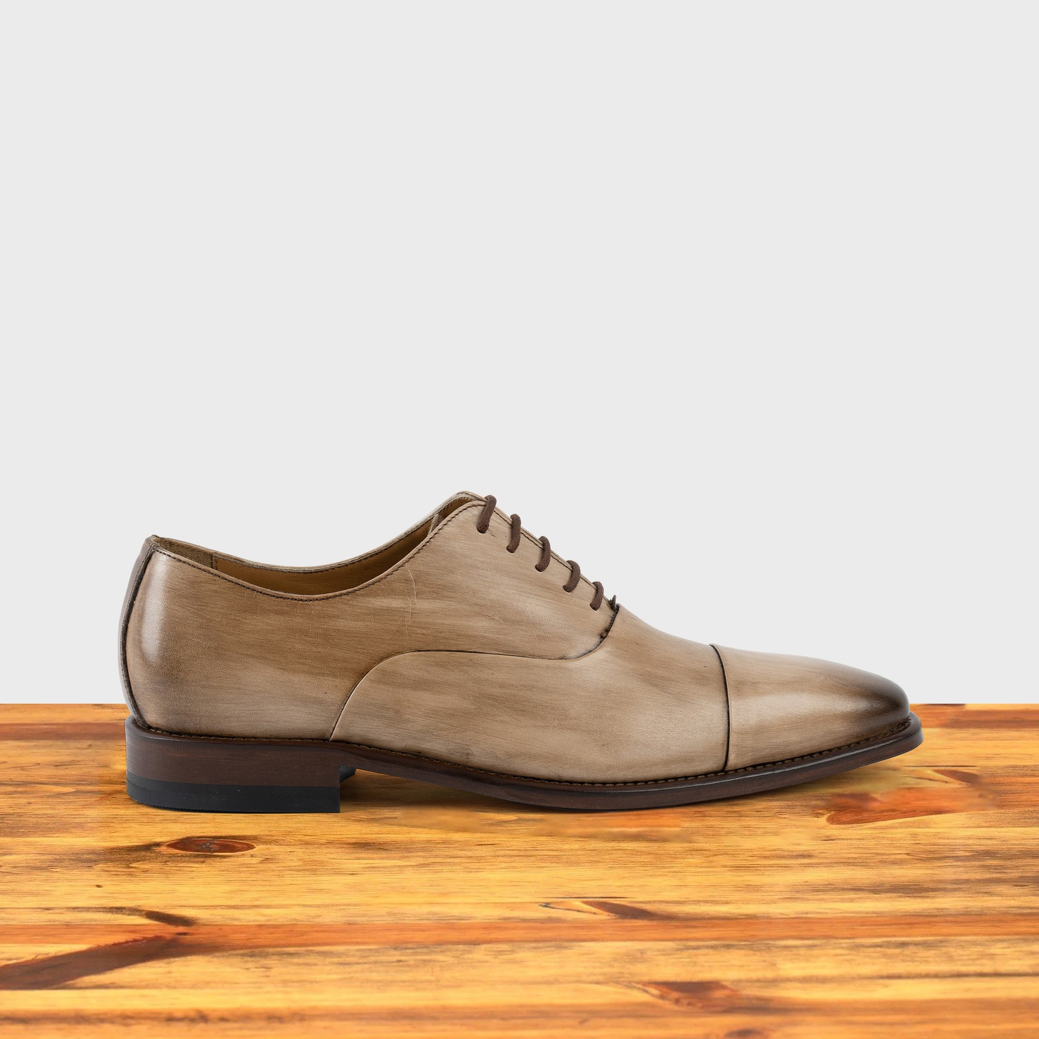 Straw leather shoe on a wooden surface with a light gray background