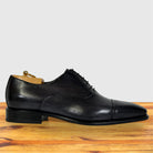 A Gray leather lace-up dress shoe with a cap toe, displayed on a wooden surface against a light gray background.