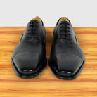 A pair of men's Gray leather oxford dress shoes with a cap toe, shown from the front on a wooden surface against a light gray background.