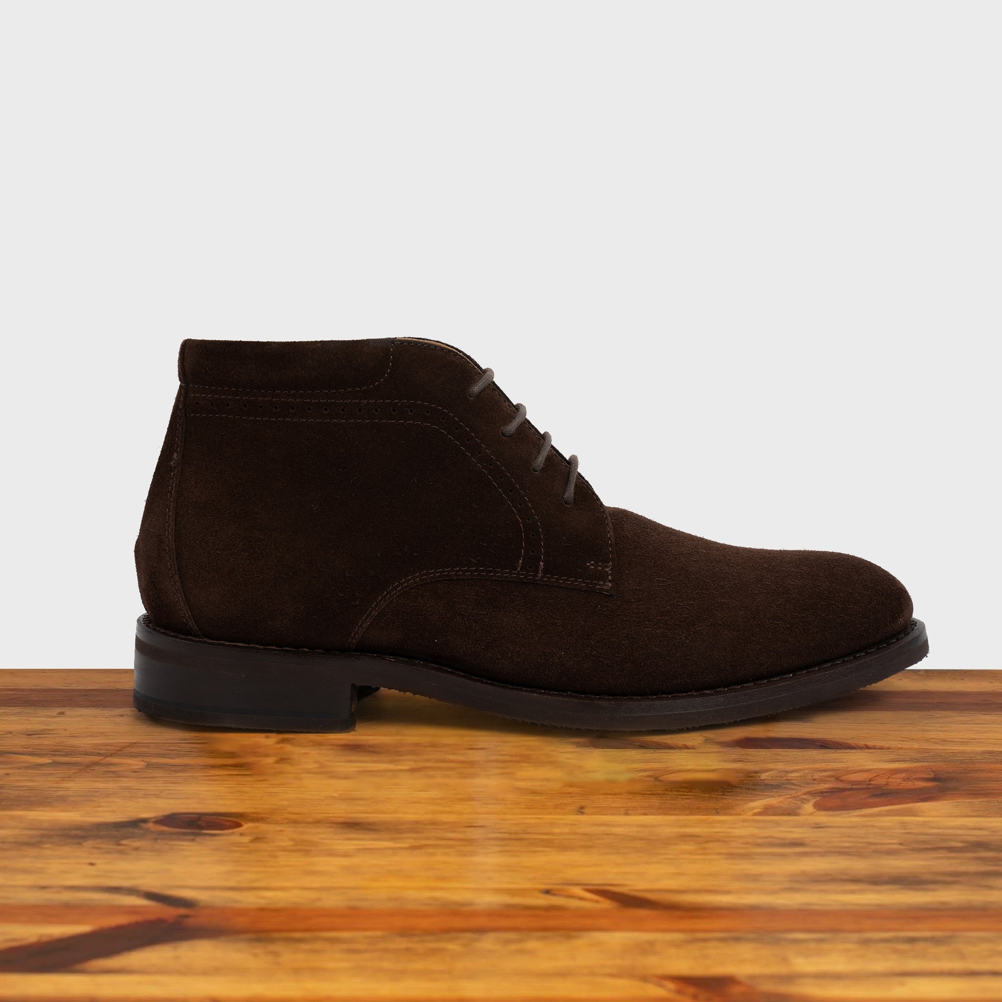 Brown suede boot on a wooden surface with a light gray background