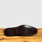 Outsole of Brown suede dress shoe on a wooden surface with a light gray background