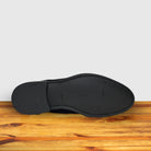 Outsole of Navy blue suede shoes on a wooden surface with a light gray background