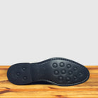 Outsole of Navy blue Chelsea boot on a wooden surface with a light gray background