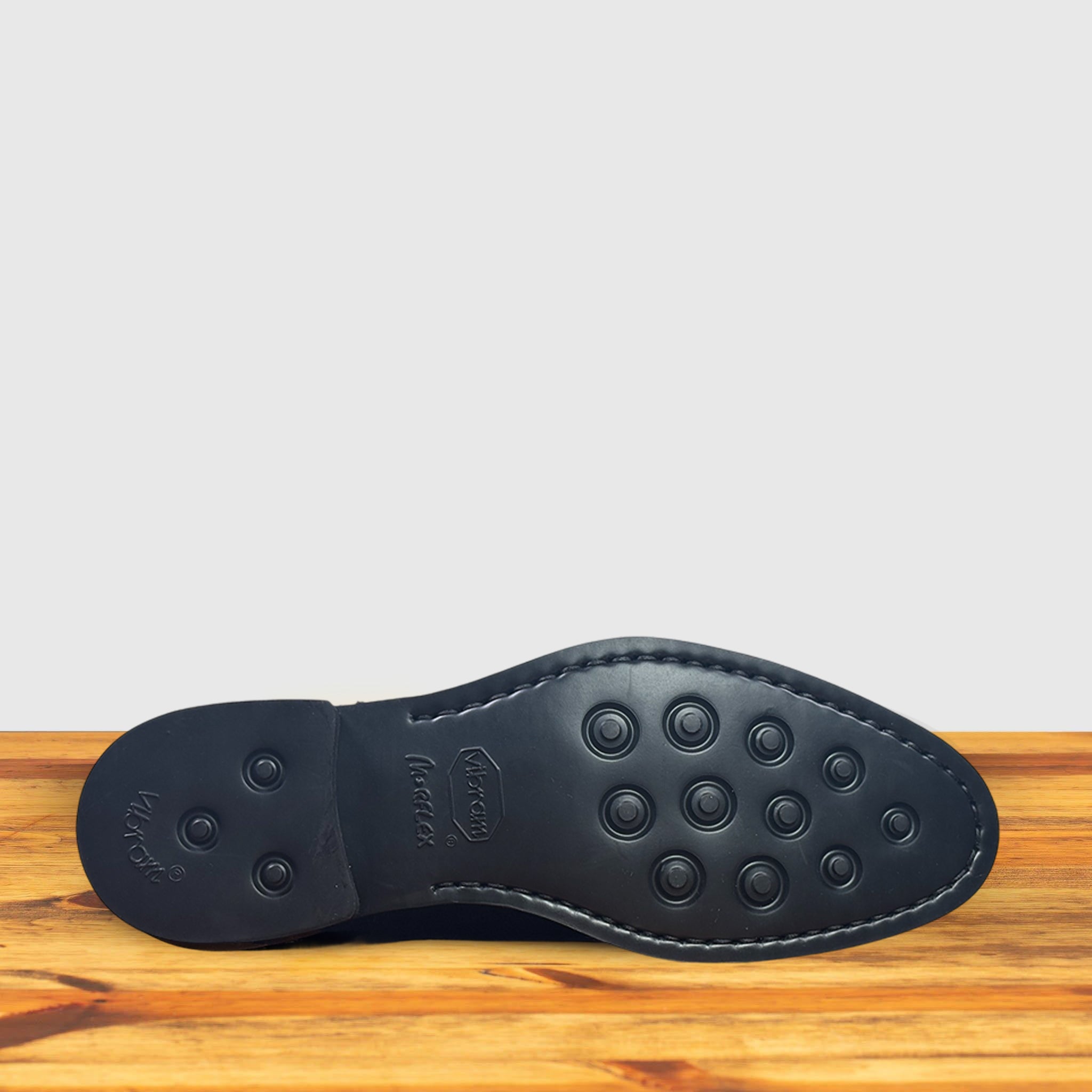 Outsole of Navy blue Chelsea boot on a wooden surface with a light gray background
