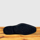 Outsole of Black leather boot on a wooden surface with a light gray background
