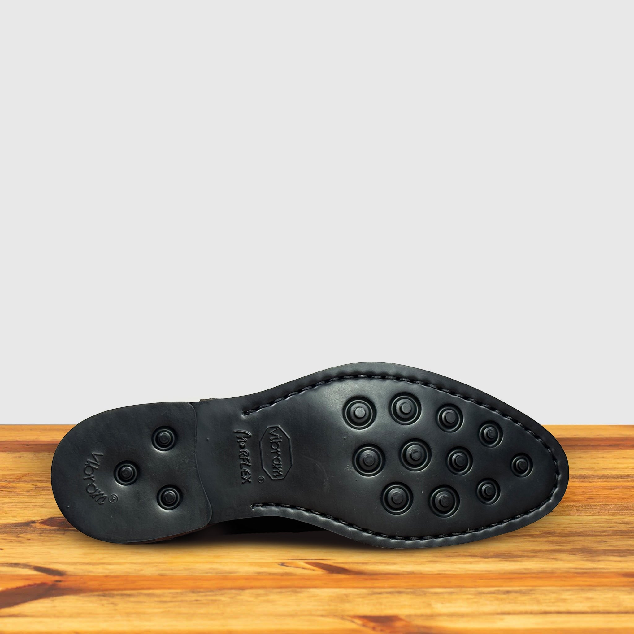 Outsole of Brown suede Chelsea boot on a wooden surface with a light gray background