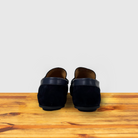 A back side of navy blue color suede penny loafer with a  strap, displayed on a wooden surface.