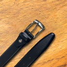 Black leather belt with silver buckle on a wooden surface