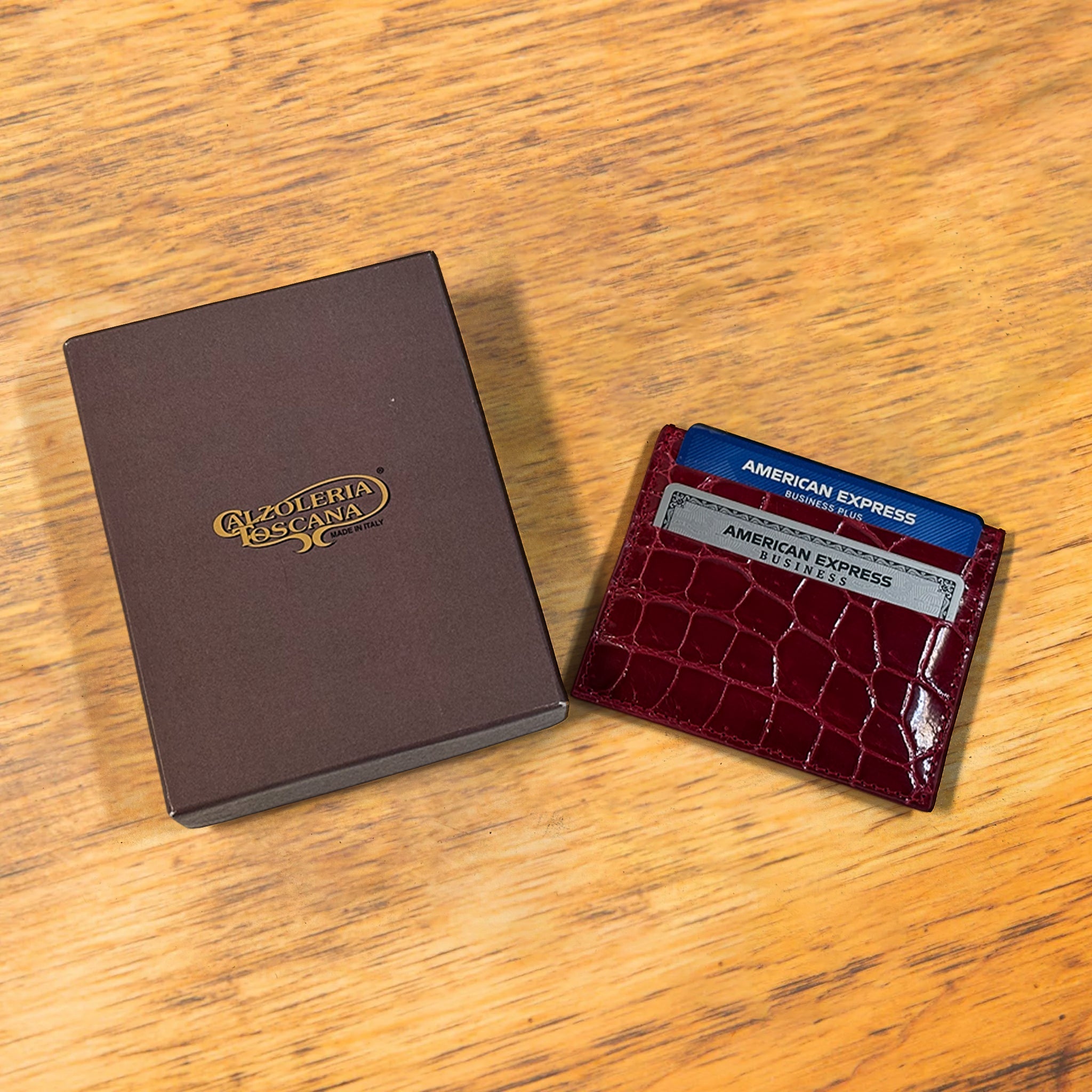 Red crocodile-patterned cardholder with credit cards and box on a wooden surface