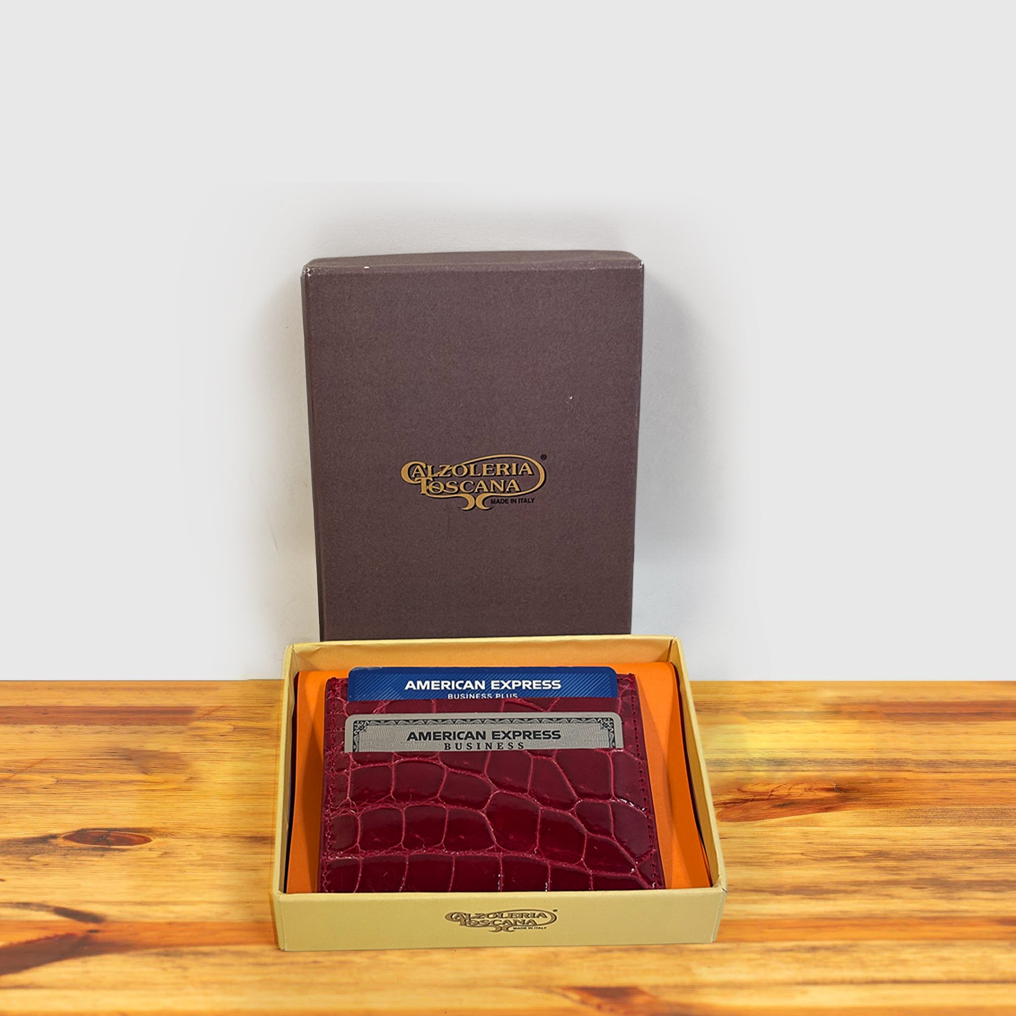 Red crocodile-patterned cardholder with credit cards and a box on a wooden surface and light gray background