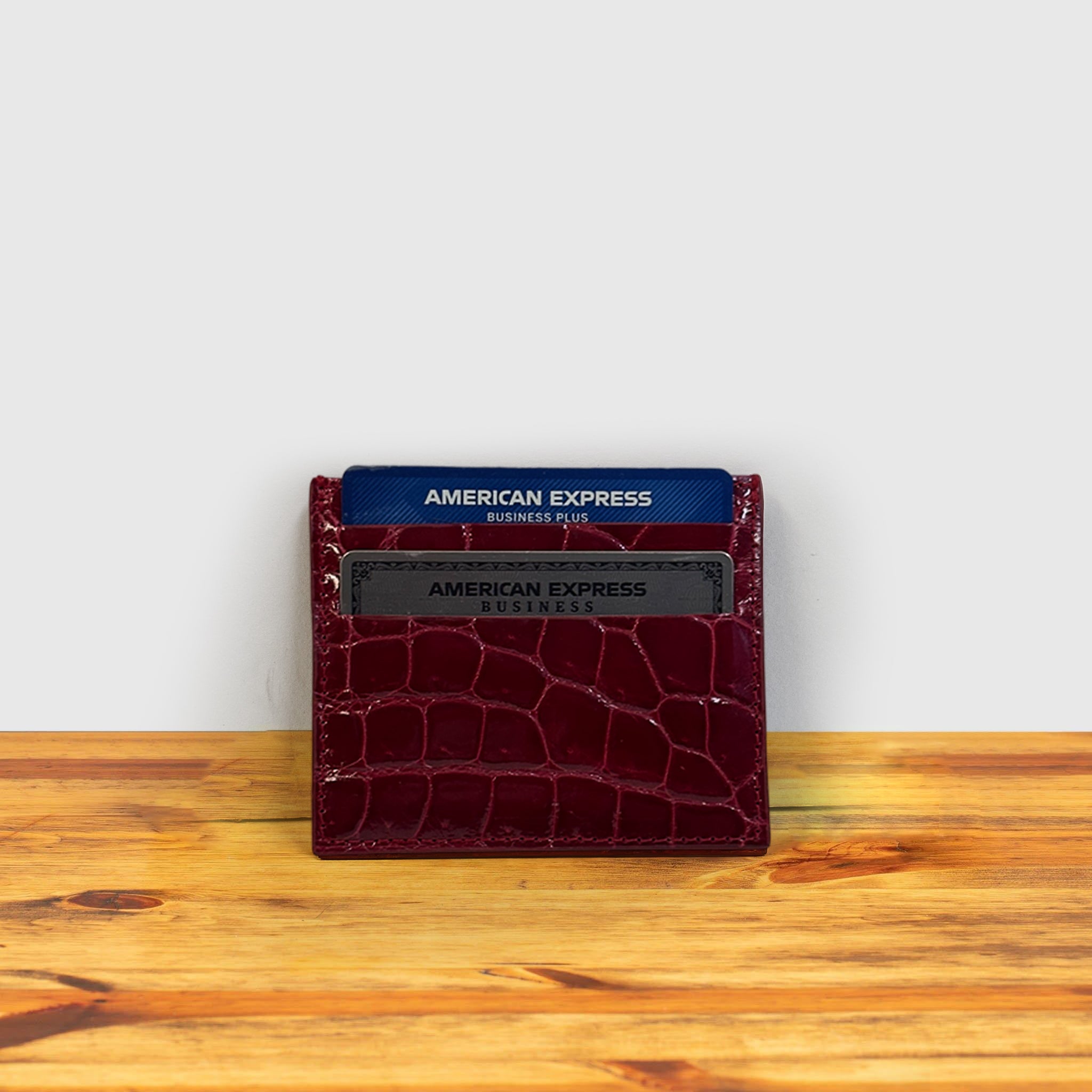 Red crocodile-patterned cardholder with American Express cards on a wooden surface and light gray background