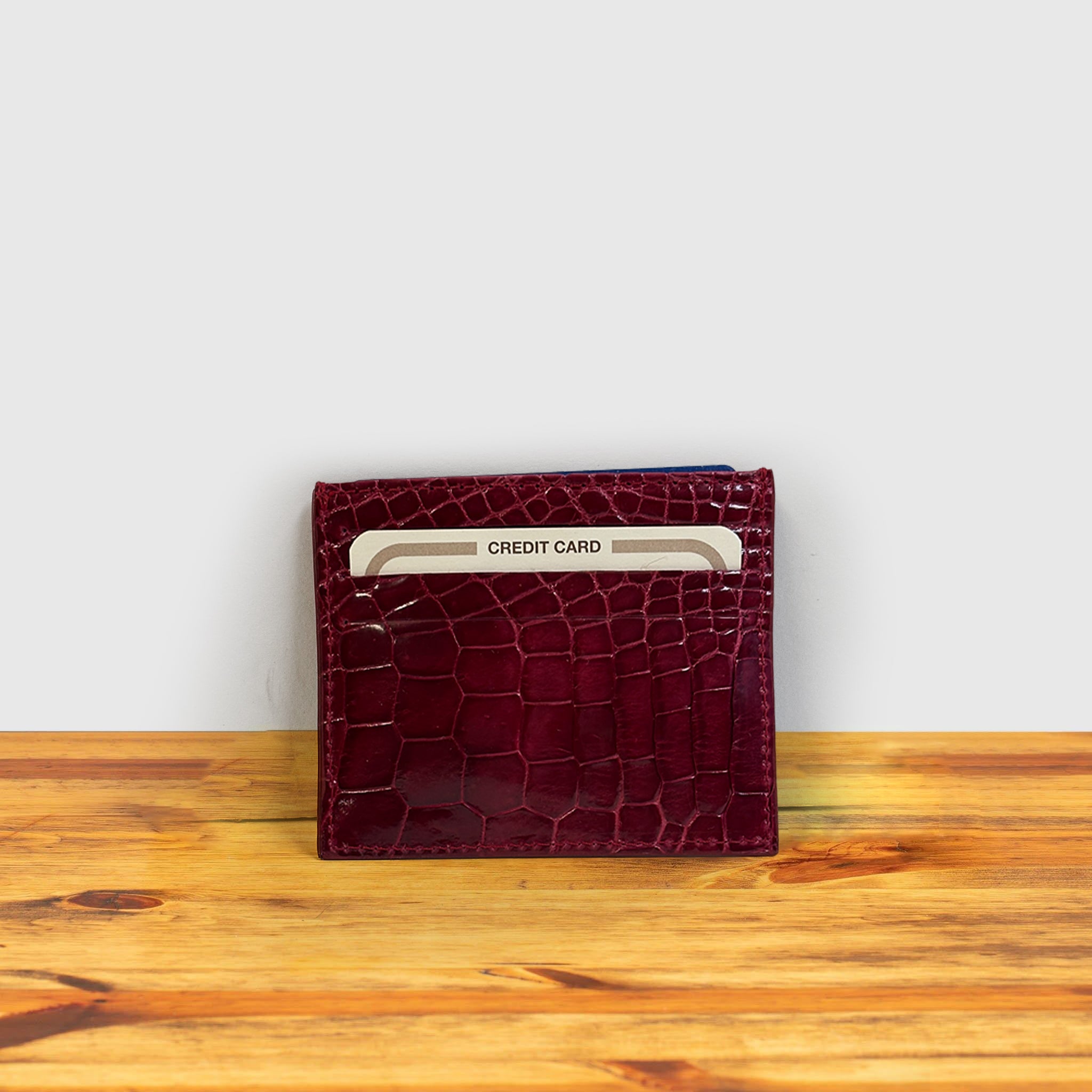 Red crocodile-patterned cardholder with credit cards on a wooden surface and light gray background