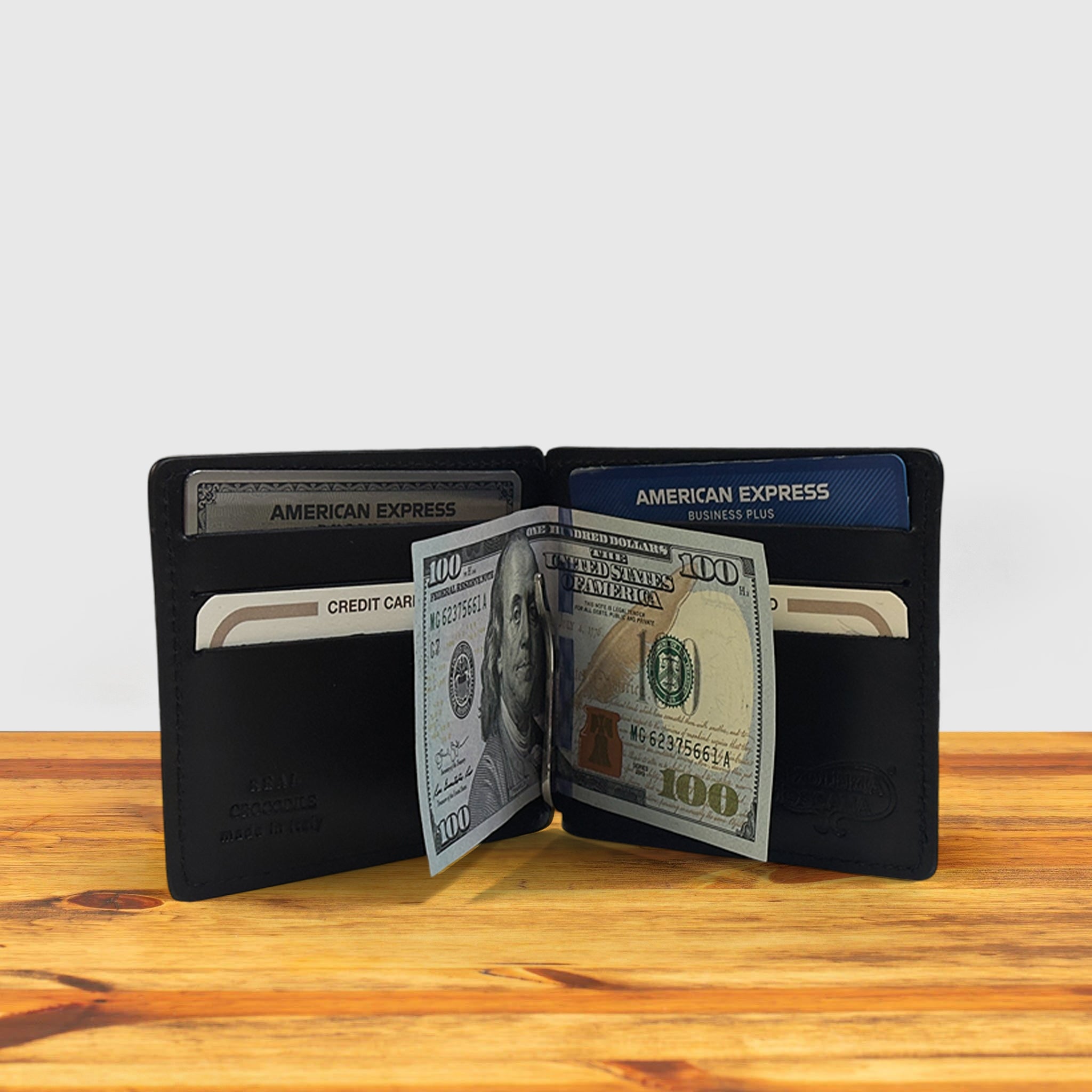 Black textured wallet on a wooden surface holiding credit cards and hundred dollar with a light gray background