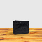 Black textured wallet on a wooden surface with a light gray background