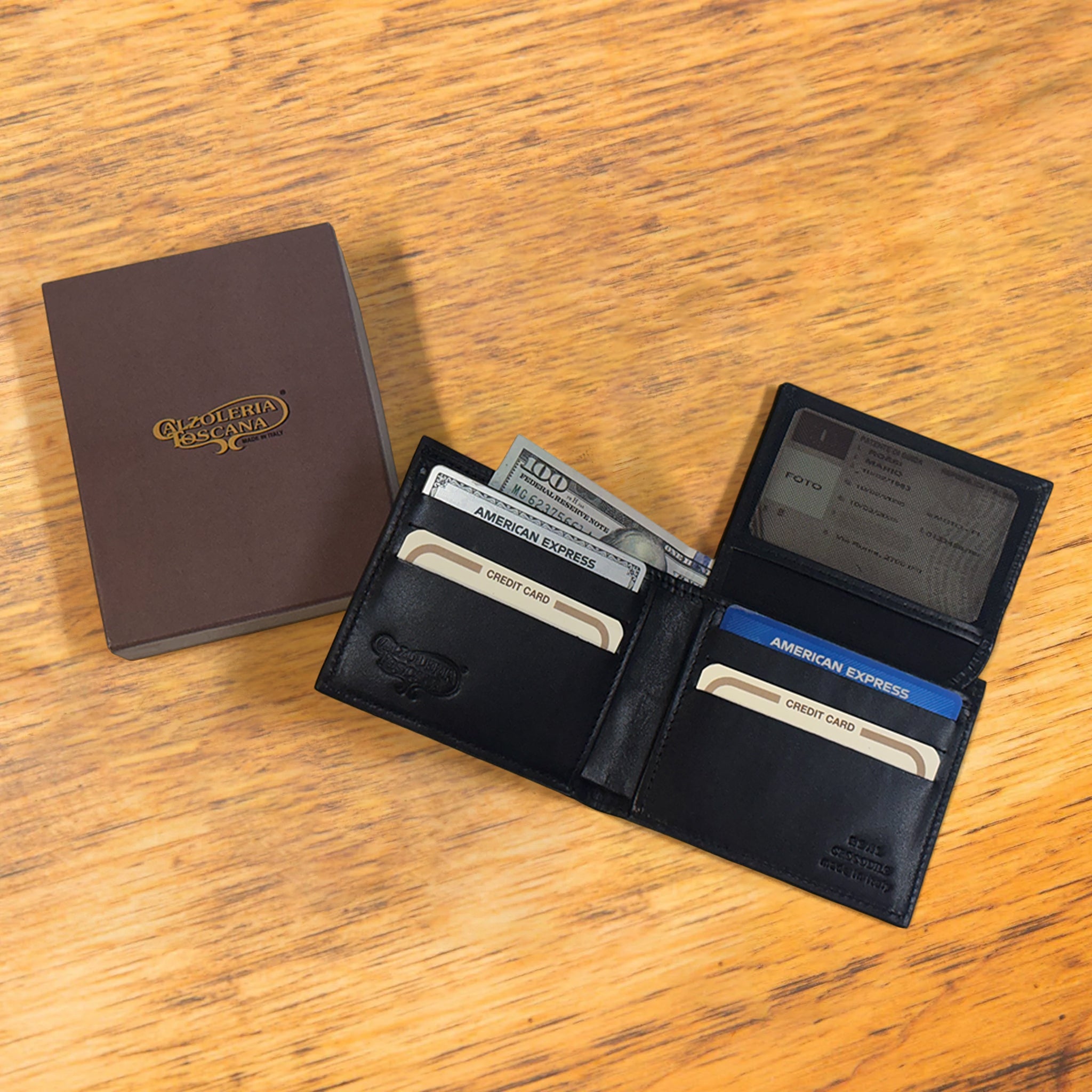 Black opened wallet  with credit cards and some cash next to box in it  at wooden surface