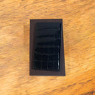 Black crocodile-patterned wallet and brown leather box on a wooden surface