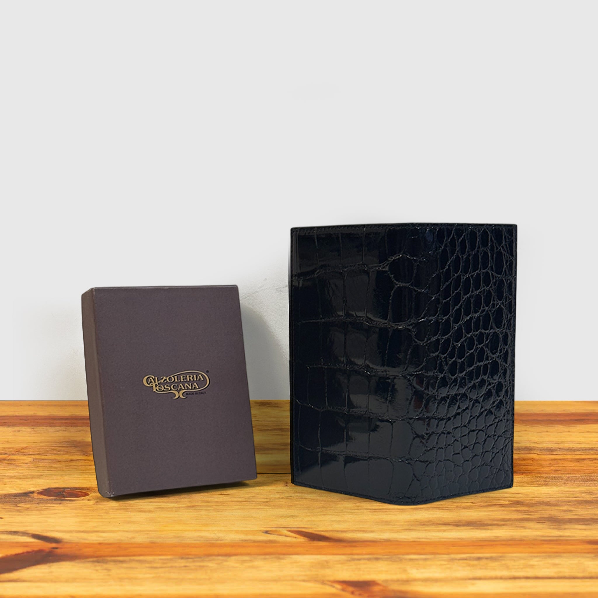 Black crocodile-patterned wallet and brown leather box on a wooden surface