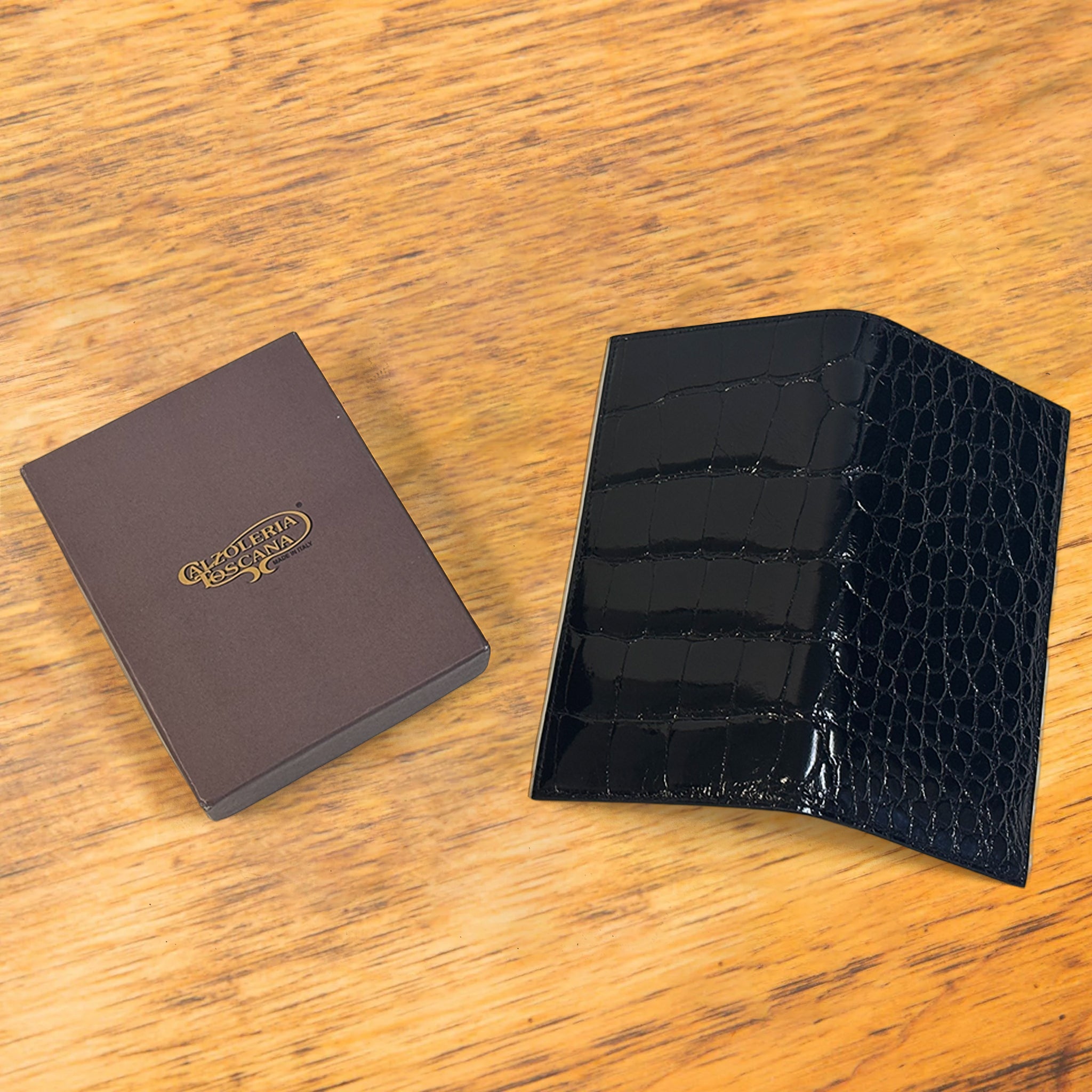 Black crocodile-patterned wallet and brown leather box on a wooden surface