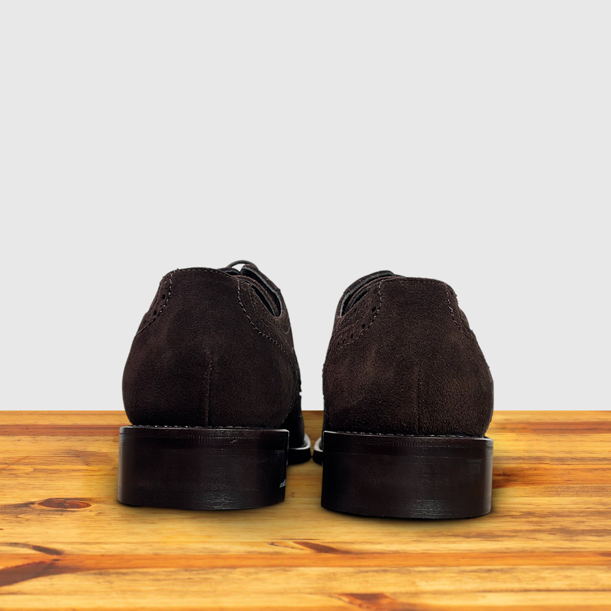 Pair of Brown suede dress shoe on a wooden surface with a light gray background