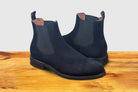Navy blue Chelsea boot on a wooden surface with a light gray background