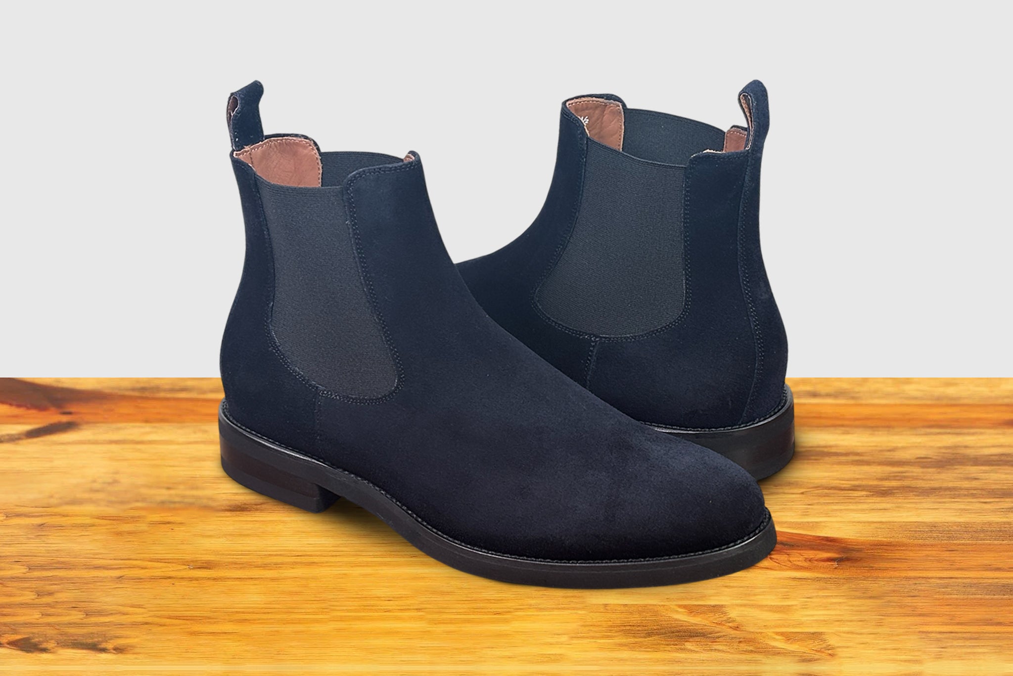 Navy blue Chelsea boot on a wooden surface with a light gray background