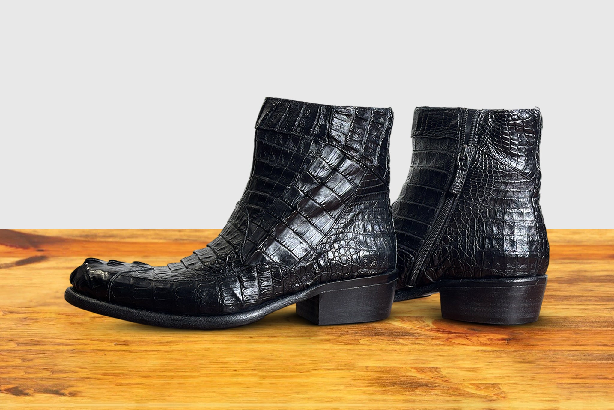 Side view of Black crocodile western boot on a wooden surface with a light gray background