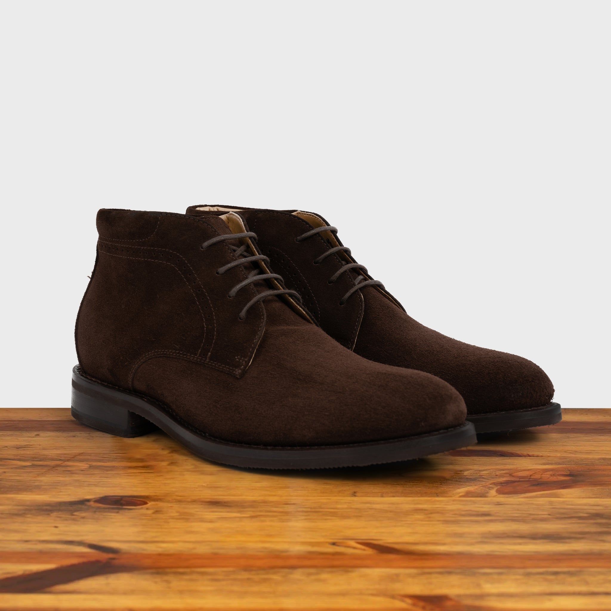 Pair of brown suede boots on a wooden surface with a light gray background