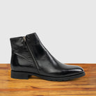 Black leather ankle boot with a zipper on a wooden surface