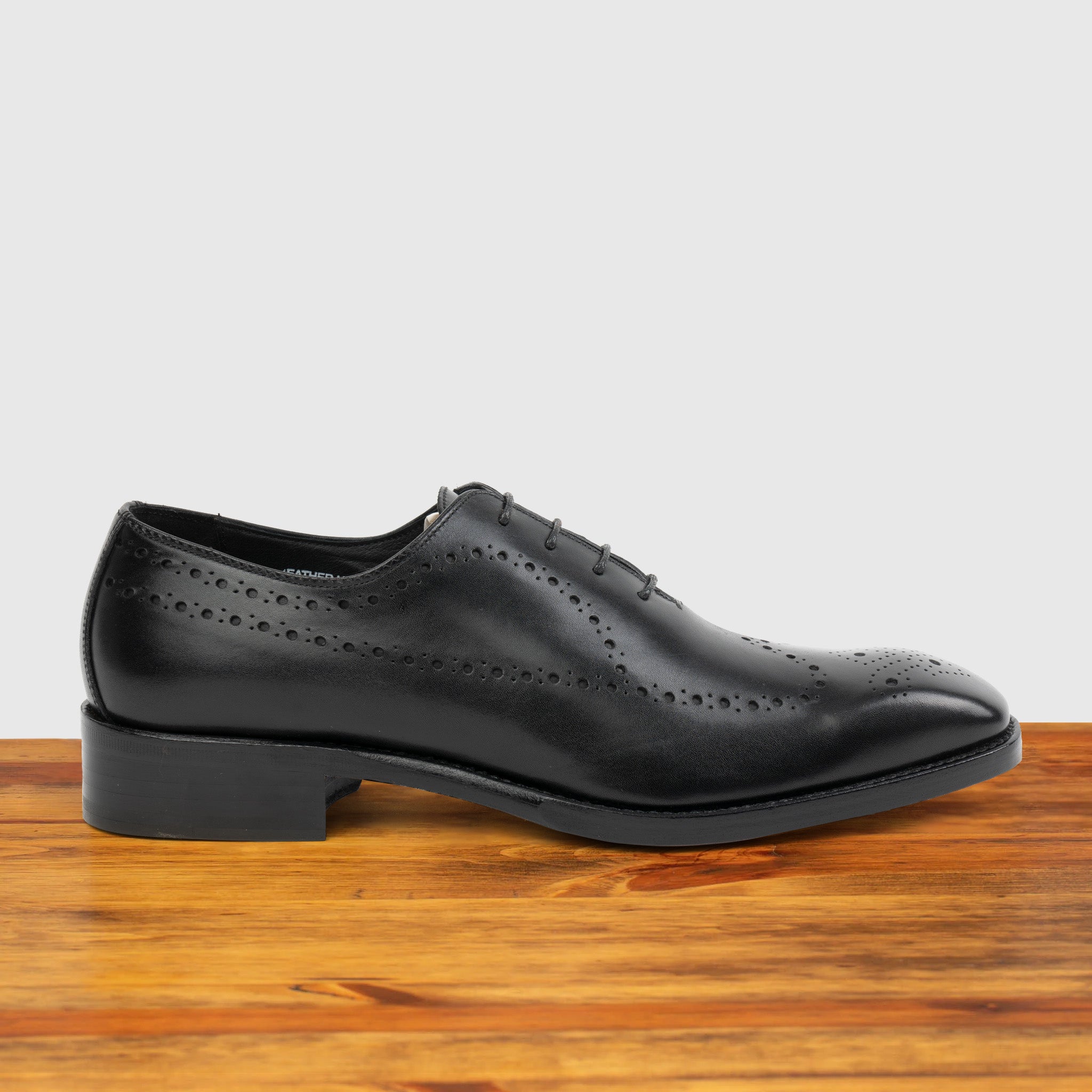 Black wholecut dress shoe on a wooden surface with a light gray background