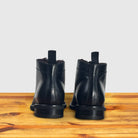 A pair of Black leather boot on a wooden surface with a light gray background