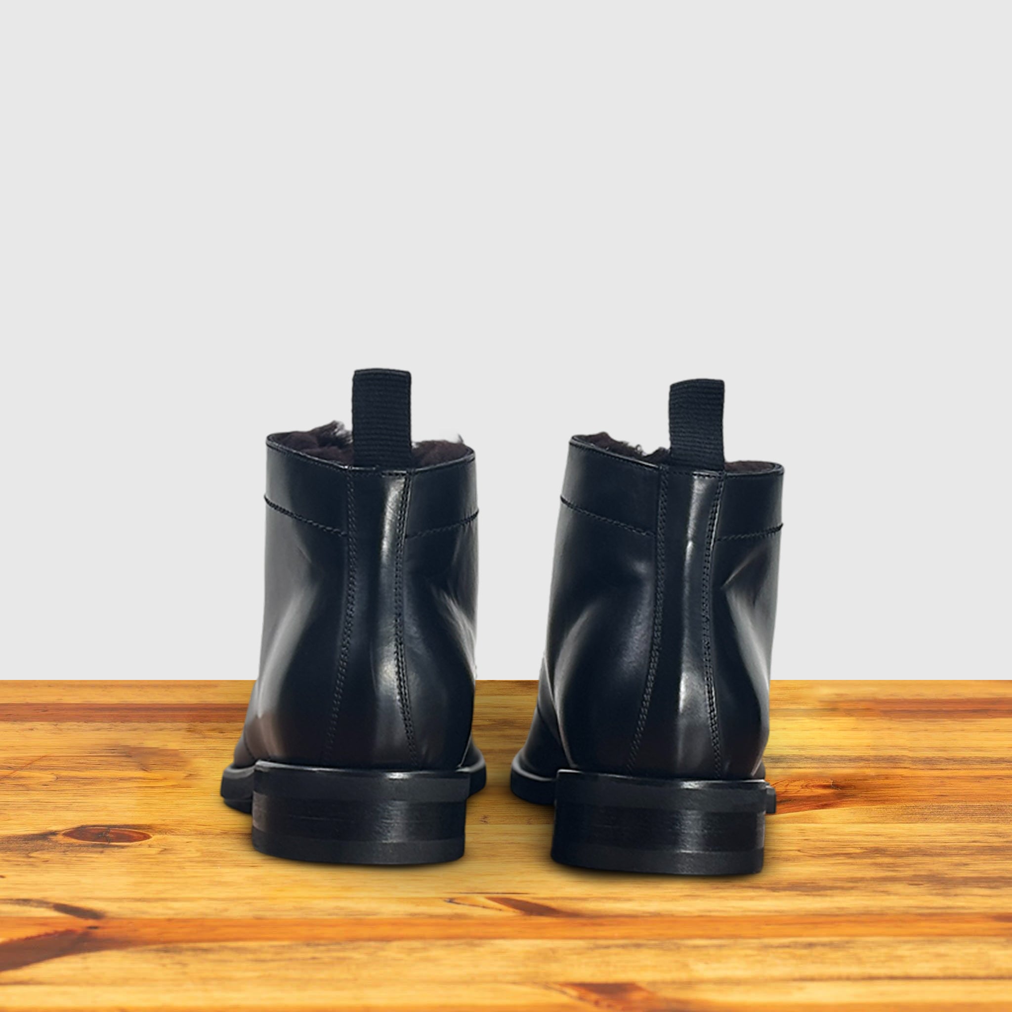 A pair of Black leather boot on a wooden surface with a light gray background