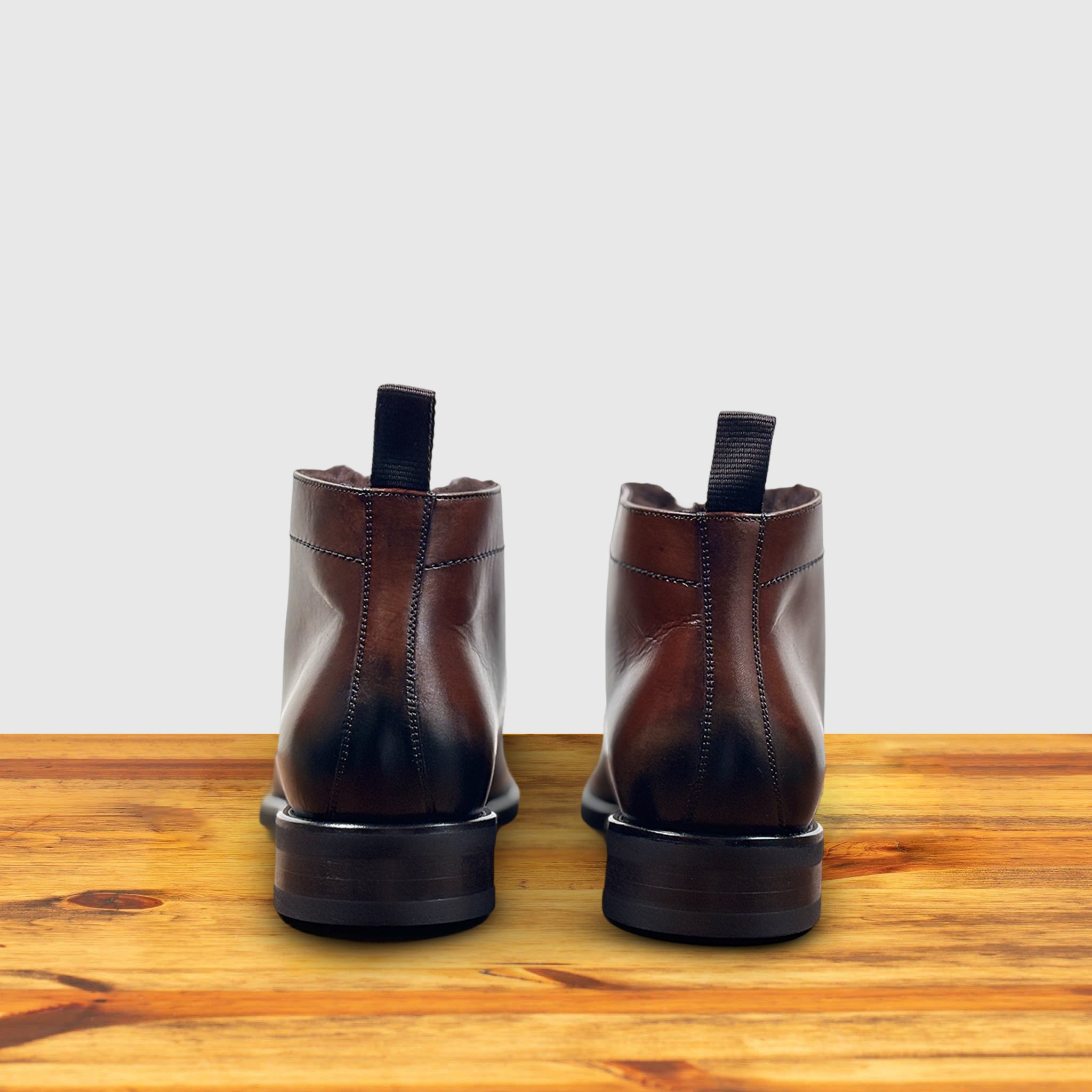 Pair of brown leather boots on a wooden surface with a light gray background
