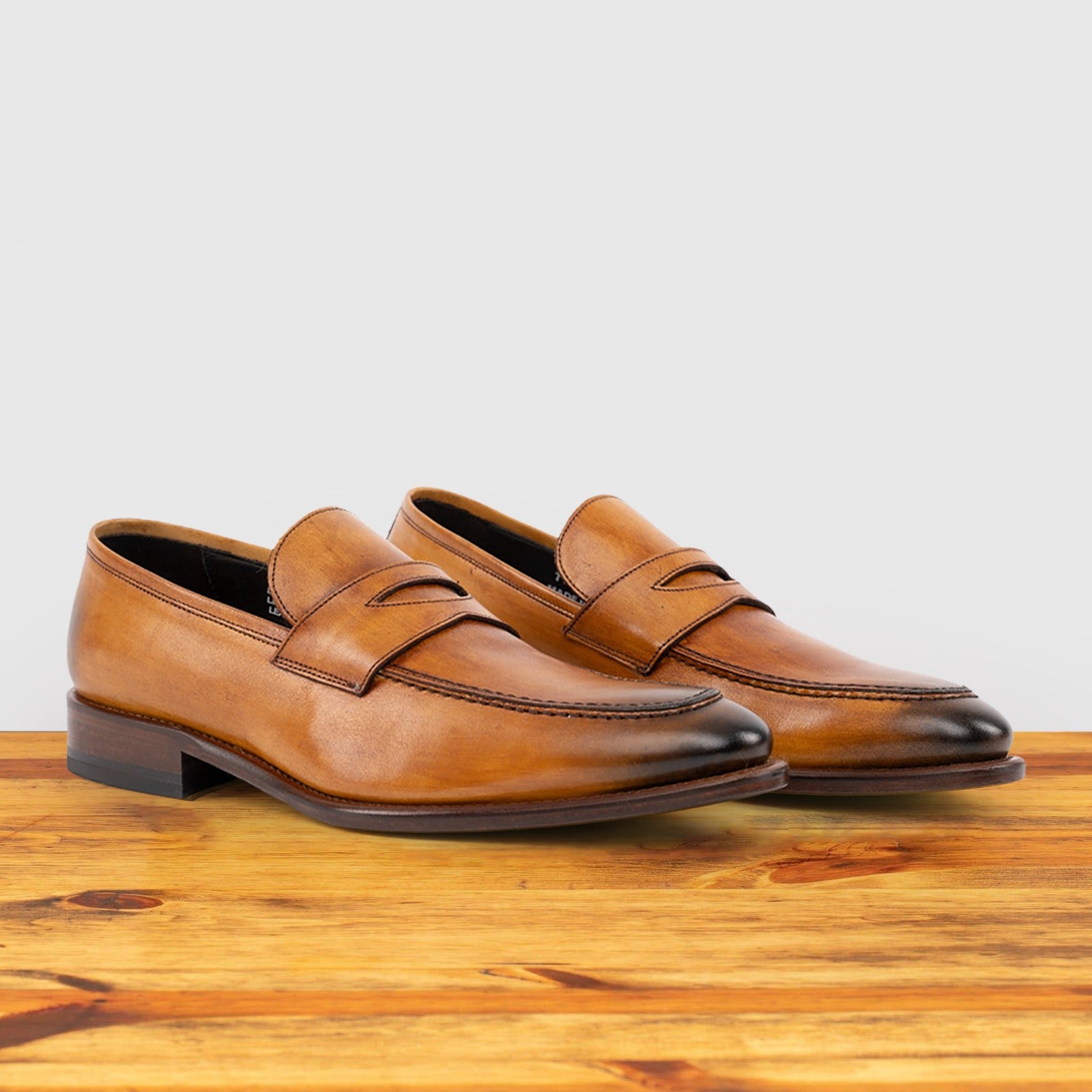 A Pair of Brown leather loafer on a wooden surface with a light gray background