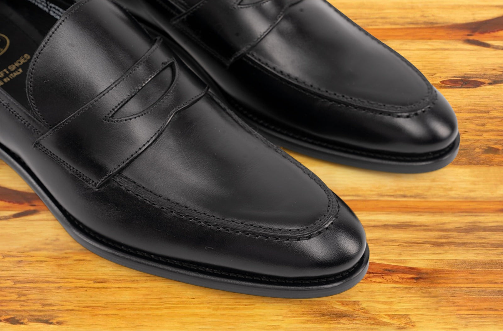 A Pair of black Italian leather dress loafer with a penny strap, on a wooden surface.