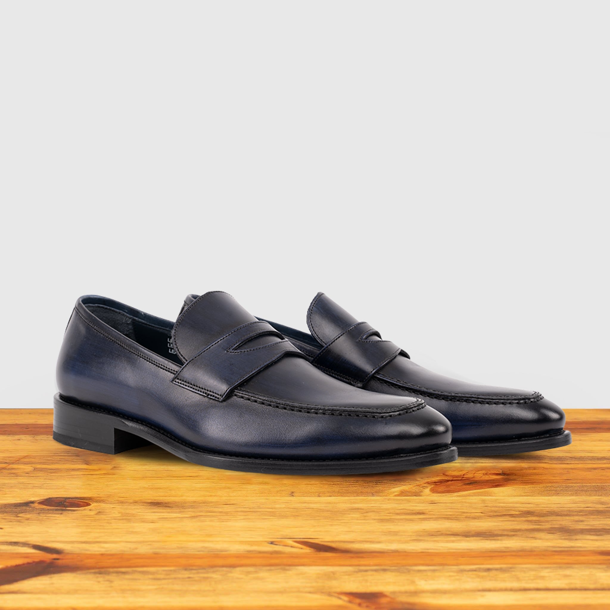 A Pair of blue Italian leather dress loafer with a penny strap, side view, on a wooden surface.