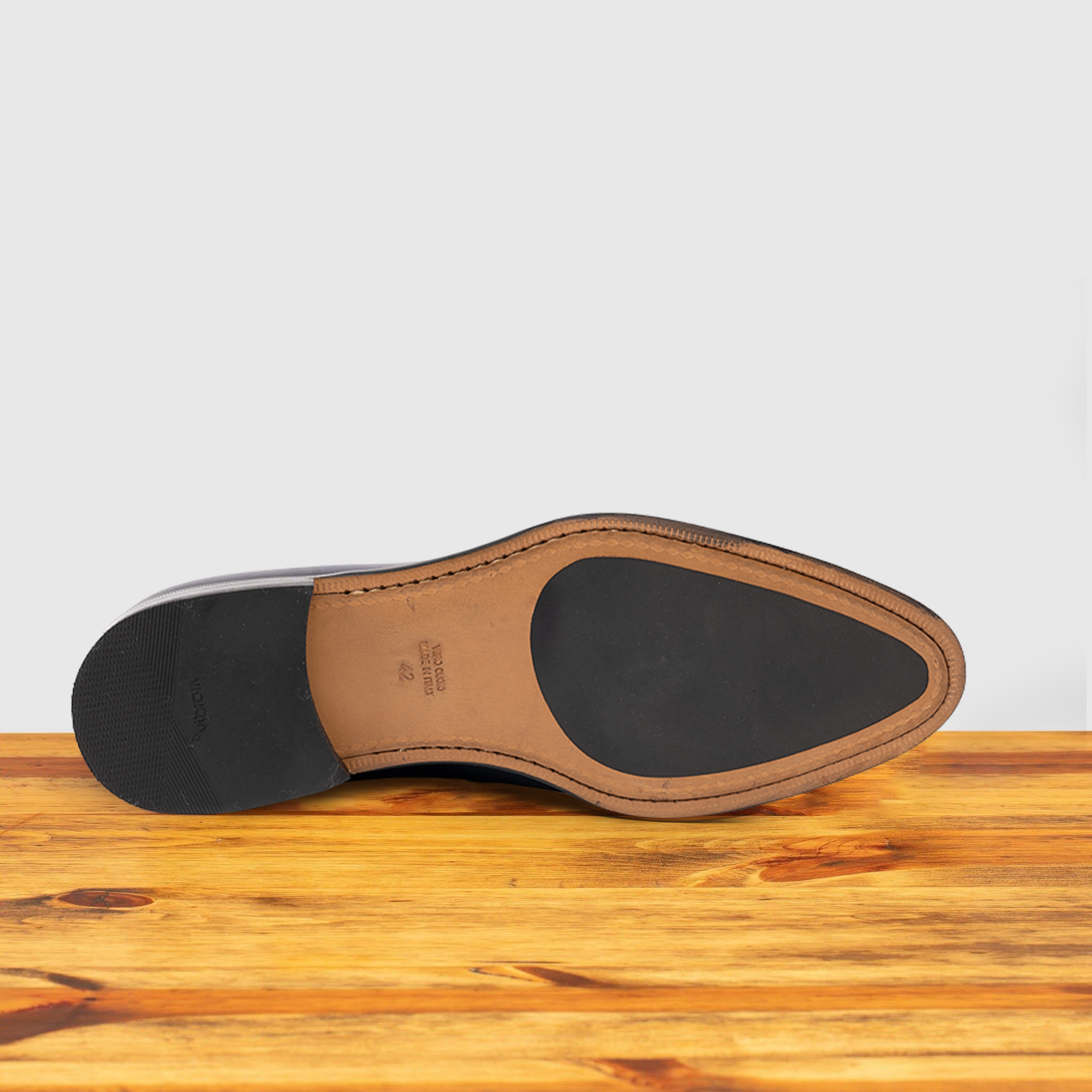 Outsole of blue Italian leather dress loafer with a penny strap, on a wooden surface.