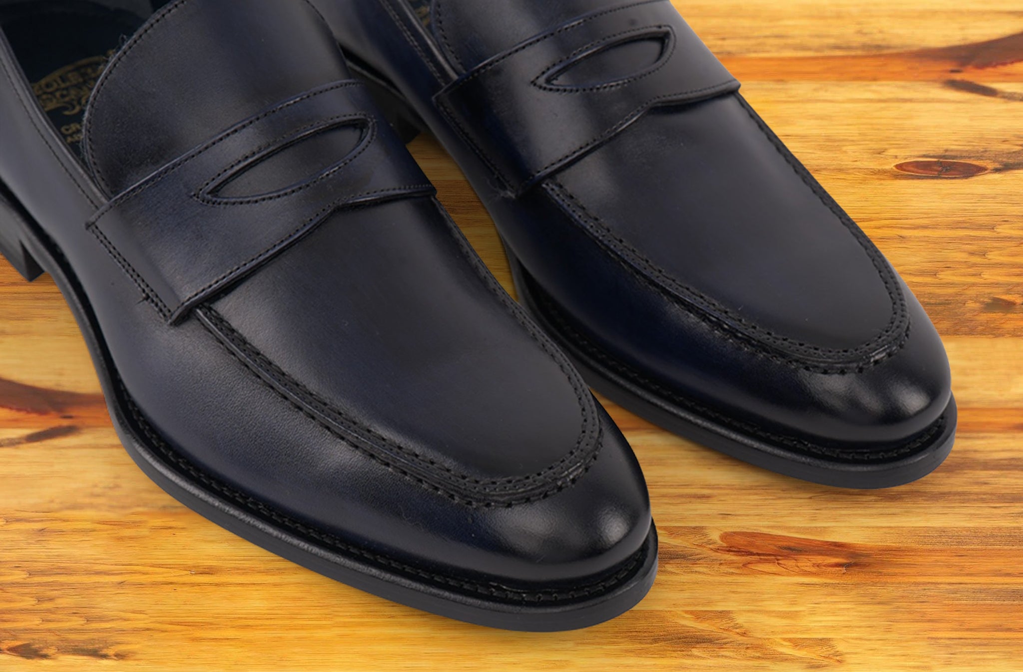 A Pair of blue Italian leather dress loafer with a penny strap, on a wooden surface.