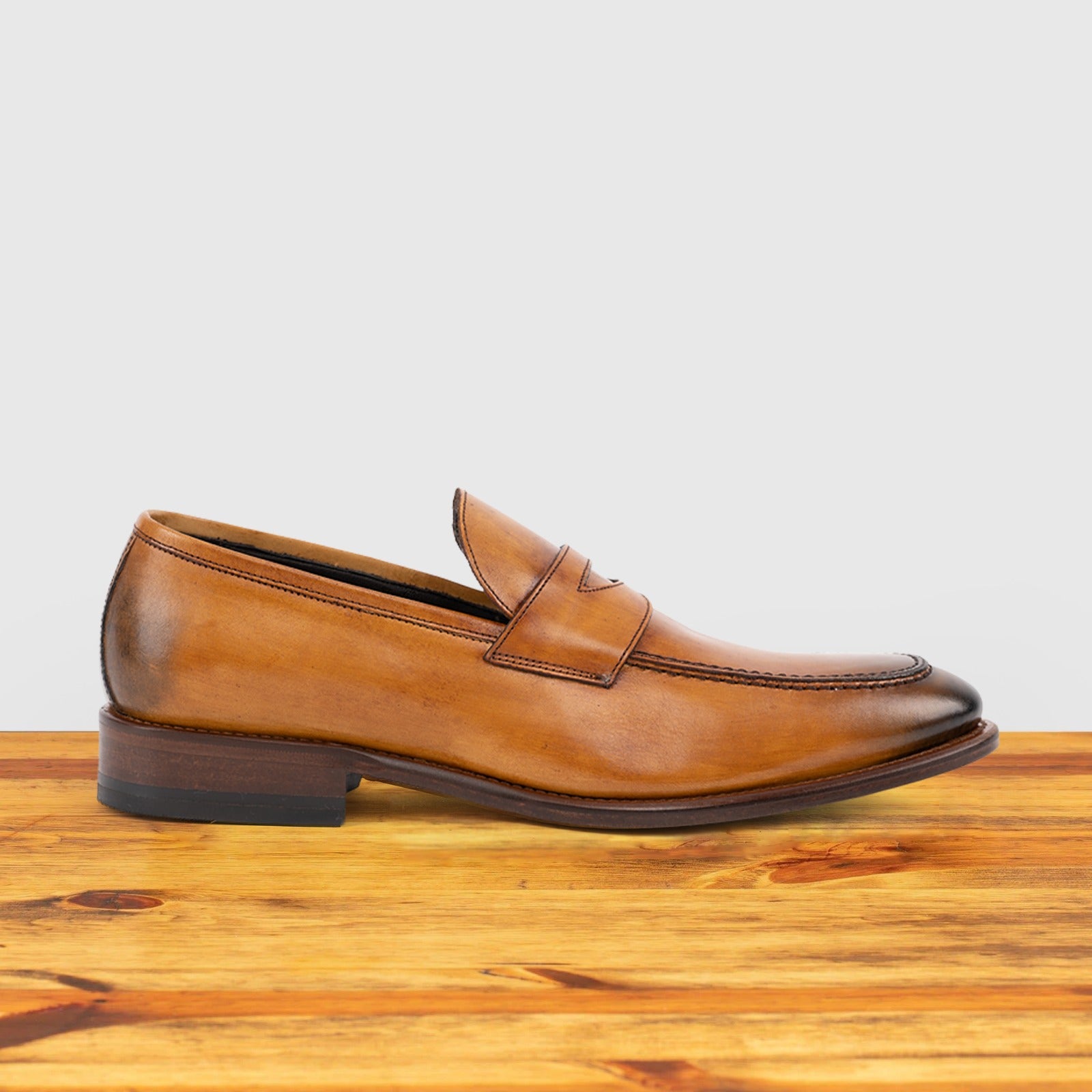 Brown leather loafer on a wooden surface with a light gray background