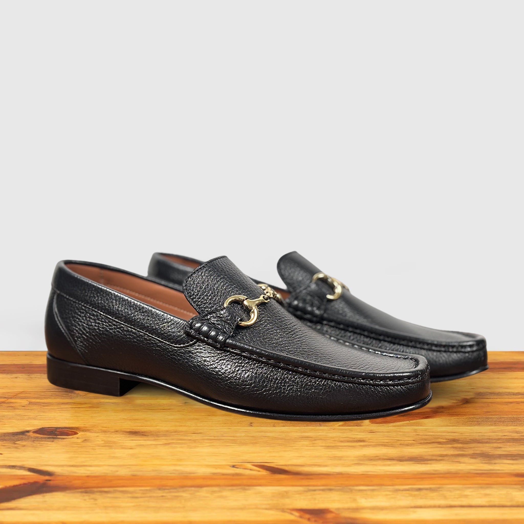 A pair of Black leather loafer with a gold buckle on a wooden surface