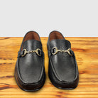 A pair of Black leather loafer with a gold buckle on a wooden surface in a light gray background