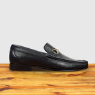 Black leather loafer with a gold buckle on a wooden surface