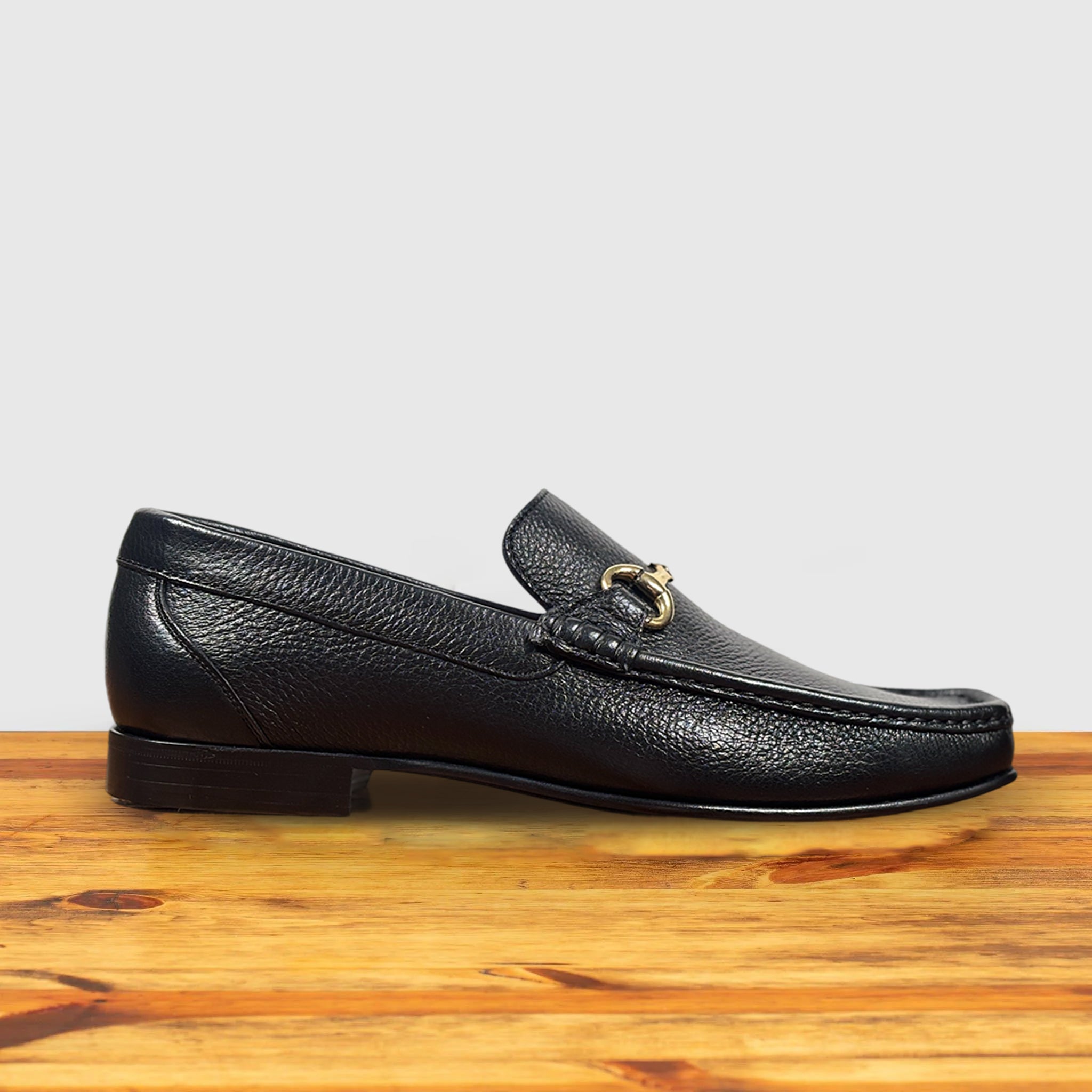 Black leather loafer with a gold buckle on a wooden surface