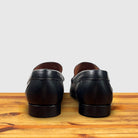 A pair of Black leather loafer with a gold buckle on a wooden surface in a light gray background