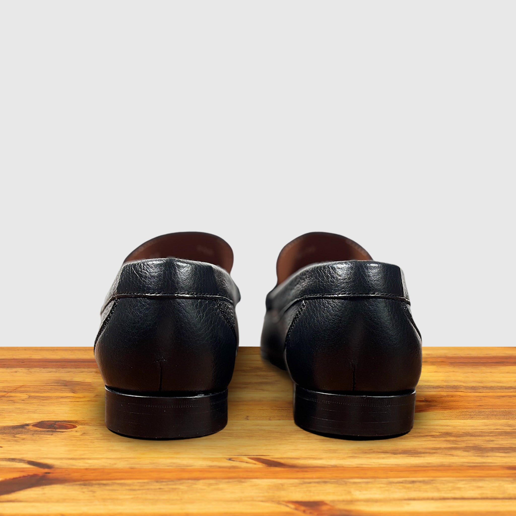 A pair of Black leather loafer with a gold buckle on a wooden surface in a light gray background
