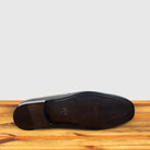 Outsole of Black leather loafer with a gold buckle on a wooden surface