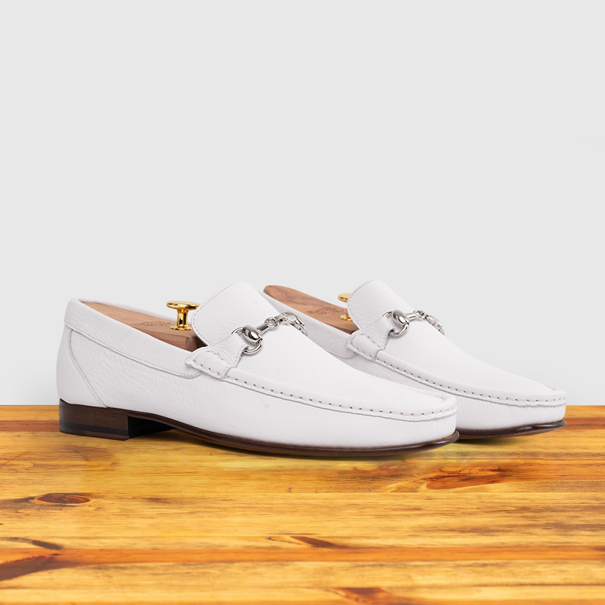 Pair of White loafer shoe on a wooden surface with a light gray background