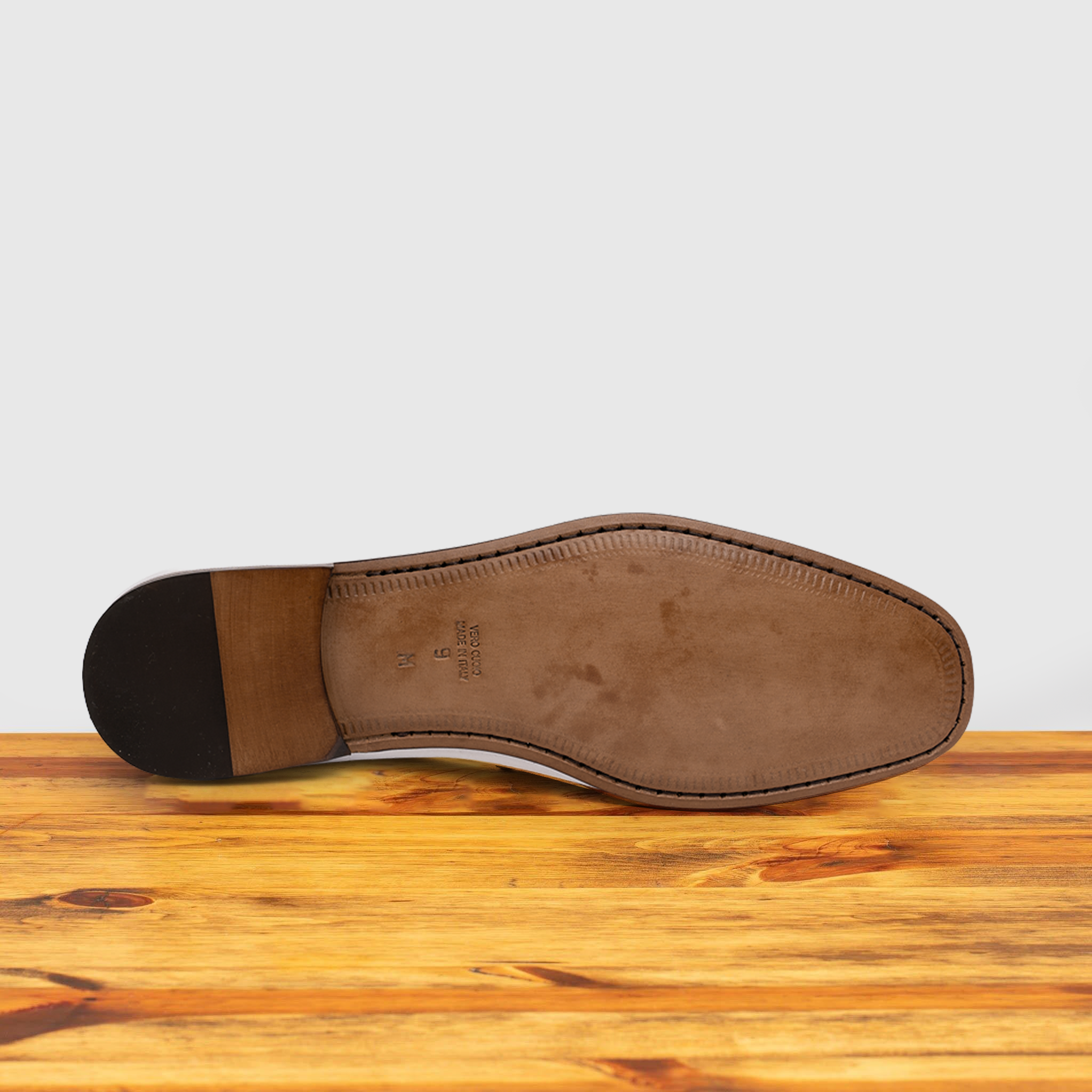Outsole of White loafer shoe on a wooden surface with a light gray background